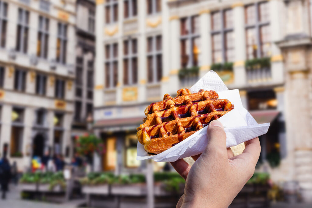 Mężczyzna trzyma w ręku popularne uliczne jedzenie - tradycyjny belgijski deser - smaczny gofr z sosem czekoladowym na tle turystycznych ulic Brukseli, Belgia, Europa.