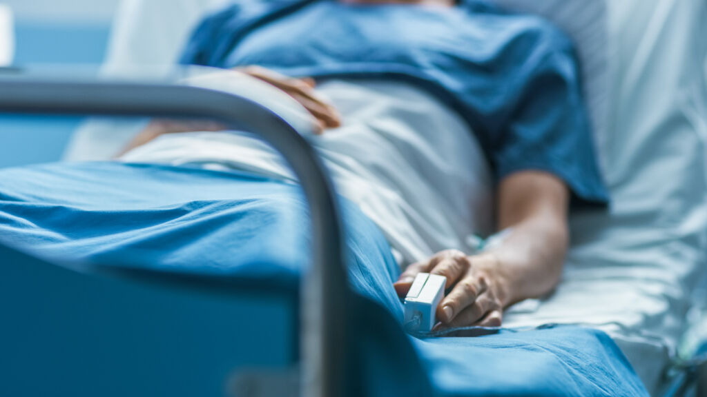 W szpitalu chory męski pacjent śpi na łóżku. Sprzęt monitorujący tętno jest na jego palcu.