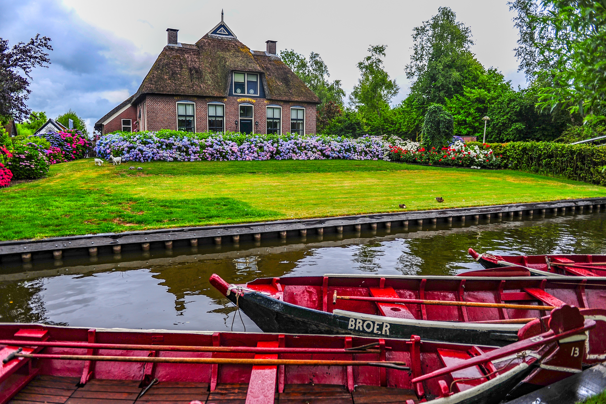 Giethoorn, Holandia - 6 lipca 2019 r: Czerwone łodzie zadokowane w kanale przed typowym holenderskim wiejskim domem w wiosce Giethoorn w Holandii