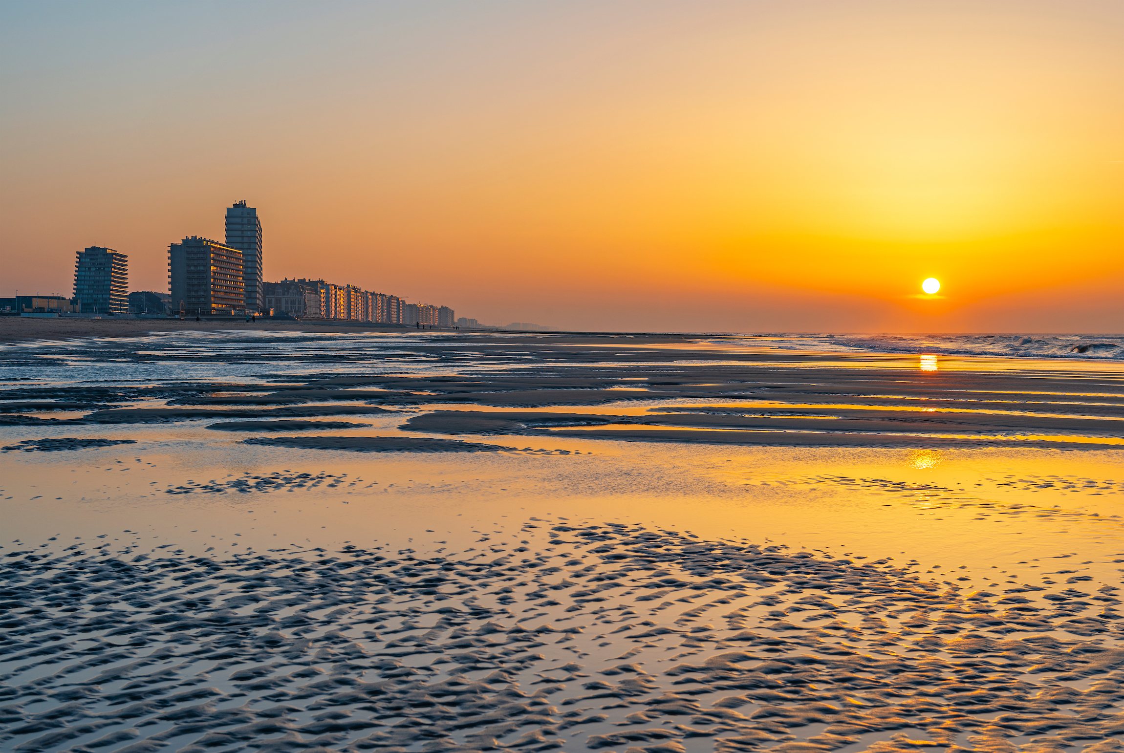 Plaża w mieście Ostenda o zachodzie słońca z nieostrym pierwszym planem nad Morzem Północnym z miejską panoramą apartamentów z widokiem na morze, Zachodnia Flandria, Belgia.