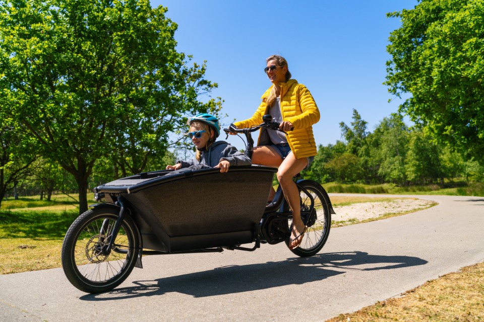 Mother and daughter having a ride on road with electric cargo bike. 
