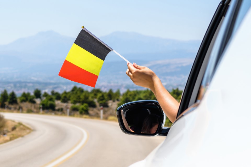 Woman holding Belgium flag from the open car window driving along the serpentine road in the mountains. Concept